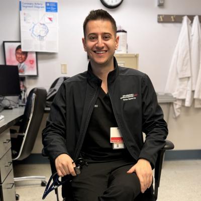 Nicholas Maalouf smiles at the camera while sitting in a chair in a medical office