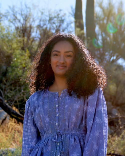 Shaela Patel standing in front of a cactus and bushes wearing a blue dress