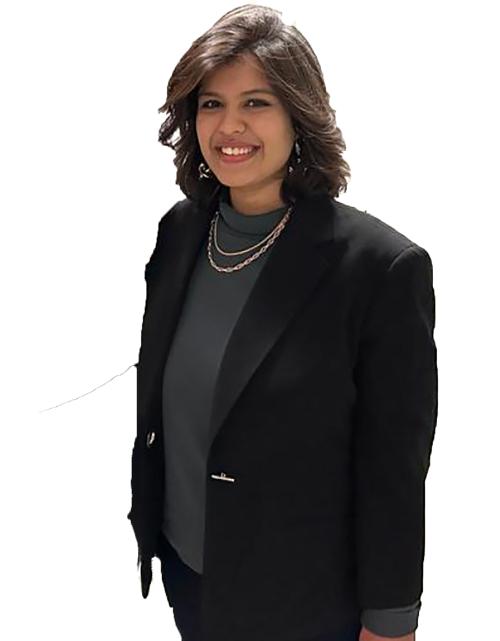 A woman with a black blazer and a pearl necklace stands smiling against a white background.