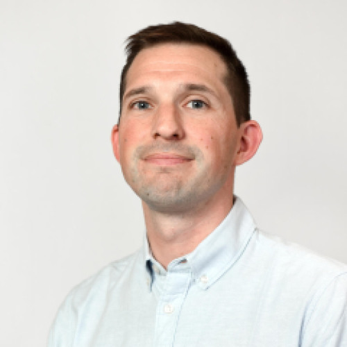 headshot of Connor Dolan, a Caucasian man with brown hair slightly smiling, wearing a light blue button down shirt in front of a white background
